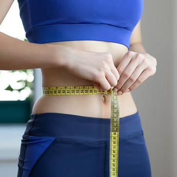 Person measuring waist with a yellow tape measure, wearing a blue athletic outfit.