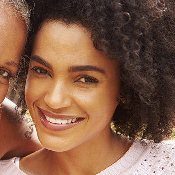 Two women smiling, one with curly hair and a white top, the other partially visible.